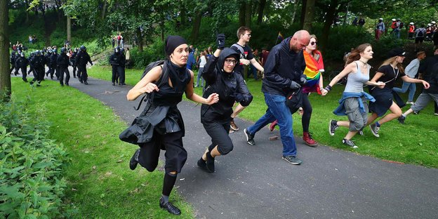 Demonstranten rennen in einer Reihe durch eine Grünanlage