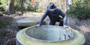 ein Mann beugt sich über einen Betonschacht im Wald