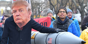 Ein Demonstrant mit riesiger Trump-Maske hält seine linke Hand stolz auf eine Pappmacheé-Atomrakete