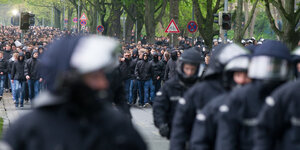 Dunkel gekleidete und teilweise vermummte Fans von Hannover 96 gehen Richtung Stadion und werden dabei von Polizisten eskortiert.