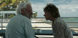 Ein älterer Mann und eine Frau sitzen auf einem Balkon am Strand und schauen sich an