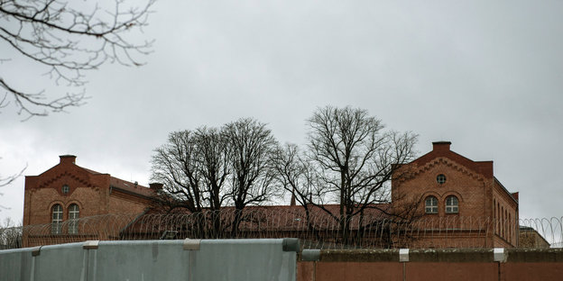 Hinter einer mit Stacheldraht gesicherten Mauer ist das Dach eines Gebäudes zu sehen