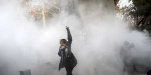 Eine einzelne Demonstrantin steht mit gereckter Faust vor einer weißen Rauchwolke