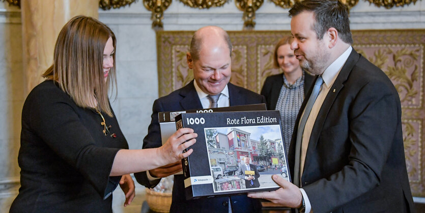 CDU-Politiker André Trepoll (rechts) überreicht Hamburgs Bürgermeister Olaf Scholz und der zweiten Bürgermeisterin Katharina Fegebank ein Puzzle, das die Rote Flora zeigt.