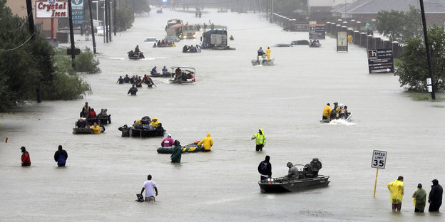 Viele Menschen stehen oder sitzen in Booten auf einer überfluteten Straße