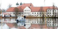 Ein Klostergebäude im Hintergrund, im Vordergrund eine überschwemmte Landschaft und ein Boot
