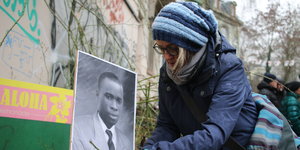 Eine Teilnehmerin der Gedenkkundgebung 2017 legt Rosen vor einem Portrait Laye Condés nieder.