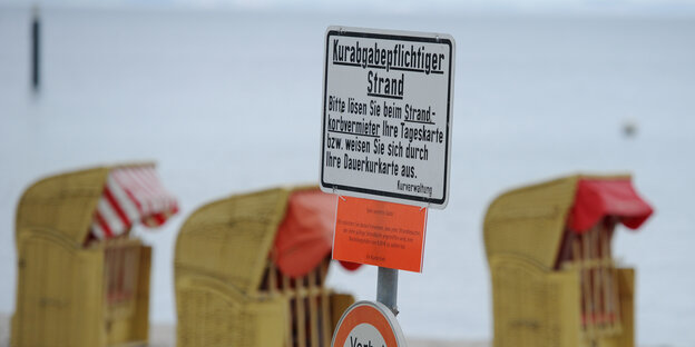 Ein Schild mit dem Hinweis auf eine kostenpflichtige Strandbenutzung steht vor drei Strandkörben.