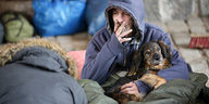 Ein Obdachloser sitzt mit seinem Hund in einem Schlafsack
