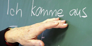 Eine Hand zeigt auf einer Schultafel den Satzteil „Ich komme aus"