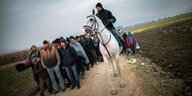 Flüchtlinge stehen auf einem Feld. Neben ihnen ein Polizist auf einem Pferd