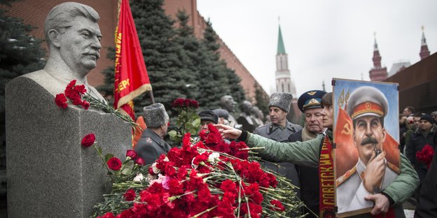 Vor einer Stalinstatue liegen rote Rosen, eine Frau hält ein Porträt von ihm im Arm