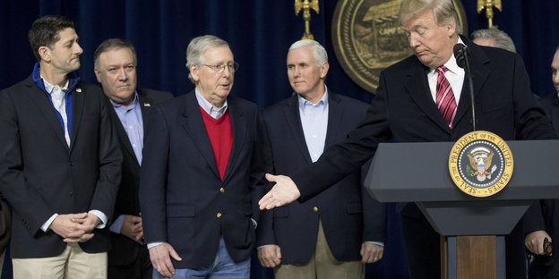 Donald Trump hinter einem Rednerpult, daneben eine Reihe Männer
