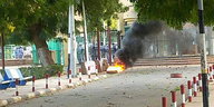 ein brennedes Objekt vor einem Eingangstor, dahinter uniformierte Polizei