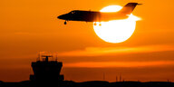 Ein Flugzeiúg sinkt vor einer rot glühenden Abendsonne