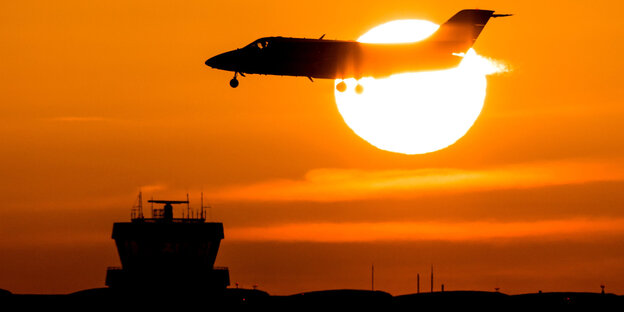 Ein Flugzeiúg sinkt vor einer rot glühenden Abendsonne