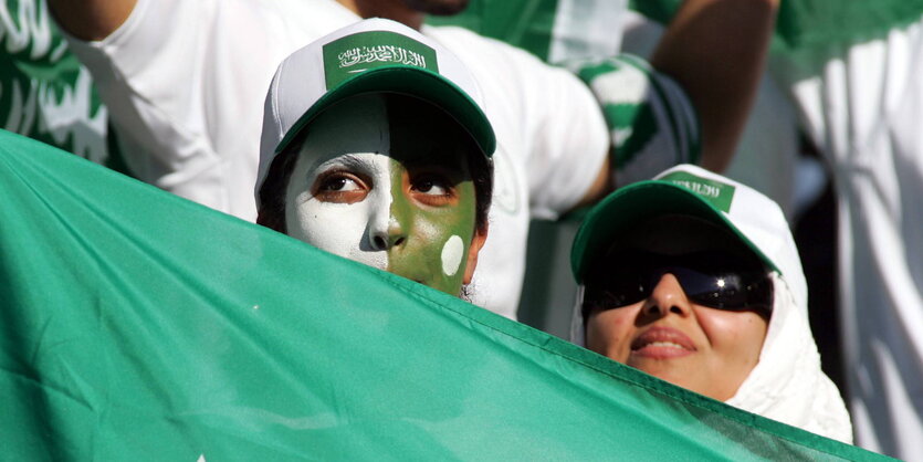 zwei weibliche Fans mit Basecaps und saudi-arabischer Fahne, eine mit grün-weiß angemaltem Gesicht