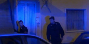 Zwei Carabinieri stehen im blauen Licht der Polizeisirenen vor einer verschlossenen Tür
