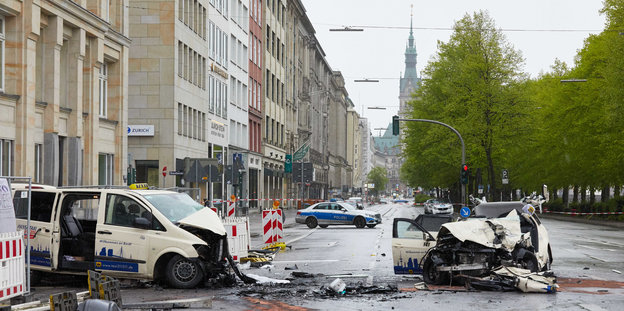Zwei demolierte, offenbar frontal ineinander gefahrene Autos stehen auf einer Hamburger Straße. Ein Polizeiauto kommt aus dem Hintergrund angefahren.