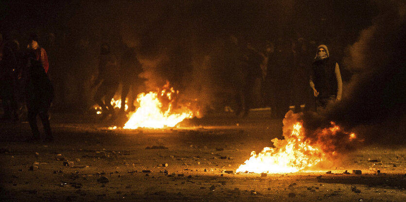 Vermummte Protestler neben offenen Feuerstellen auf der Straße