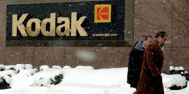 Zwei Männer im Schnee, hinten ein Kodak-Logo an einer Hauswand