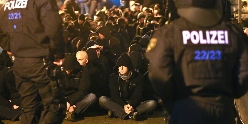 Zahlreiche Männer sitzen gefesselt vor Polizisten auf der Straße