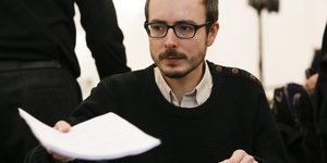 Ein Mann mit Brille hält ein Blatt Papier
