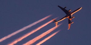 Im Licht der untergehenden Sonne zieht ein Flugzeug seine Kondensstreifen über den Himmel in Frankfurt am Main