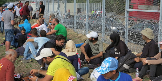 Flüchtlinge sitzen im Gras vor dem Grenzzaun in Röszke