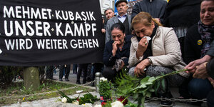 Zwei Frauen hocken vor einem Grabstein und trocknen ihre Tränen mit Taschentüchern. Es sind Angehörige des vom NSU ermordeten Kioskbesitzer Mehmet Kubasik.