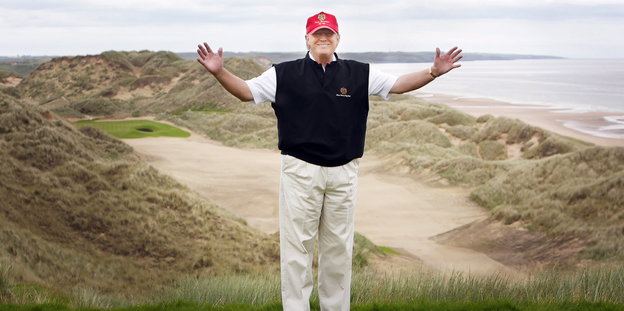 Donald Trump steht auf einem Golfplatz und hebt die Arme in die Luft