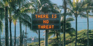Palmen und Schild mit englischsprachiger Aufschrift „Es gibt keine Bedrohung“