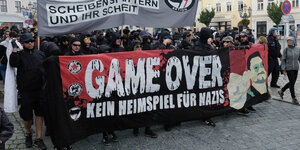 Eine Menschenmenge mit einem Transparent mit der Aufschrift "Game Over" auf einem Platz in einer Kleinstadt