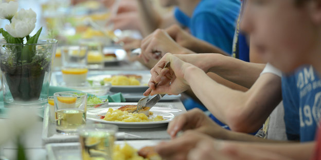 Viele Kinder und Jugendliche sitzen nebeneinander an einem langen Tisch und essen