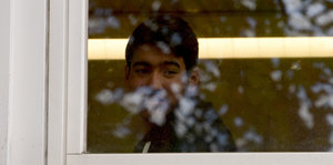 Ein Junge mit dunklen Haaren und dunklen Augenbrauen blickt aus einem Fenster.