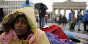 Eine Frau im Anorak sitzt auf dem Pariser Platz vor dem Brandenburger Tor in Berlin