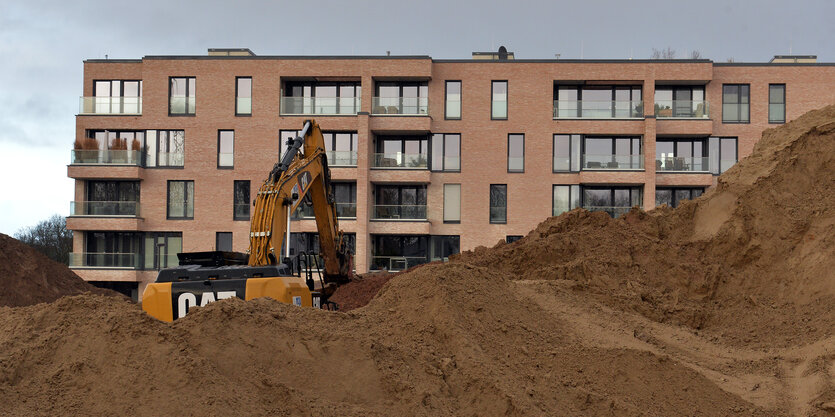 Ein Bagger steht vor einem neu gebauten Mehrfamilienhaus.