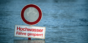 Hochwasser-Warnschild steht bis zur Kante im Wasser