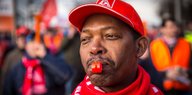 Mann mit roter Kappe und einer Trillerpfeife im Mund