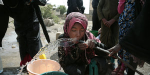 Ein Mädchen trinkt aus einem Wasserschlauch