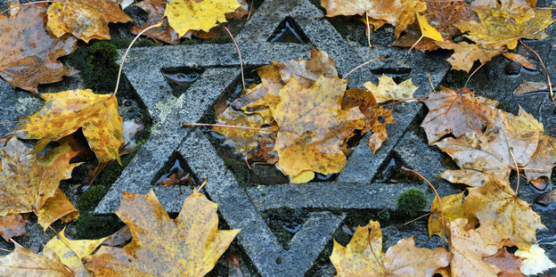 Ein Davidstern aus Stein auf dem Boden, feuchtes Herbstlaub darum herum