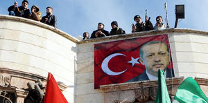 Ein Erdogan-Plakat an derFassade eines Hauses - auf dem Dach stehen Kämpfer mit Waffen