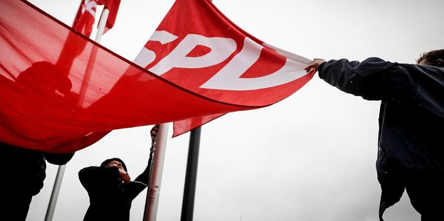 Menschen halten eine SPD-Fahne, die aufgezogen werden soll