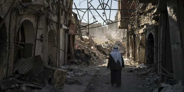 Ein Mann geht zwischen zerstörten Häusern entlang