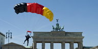 ein Fallschirmspringer mit einem schwarz-rot-goldenen Schirm landet vor dem Brandenburger Tor