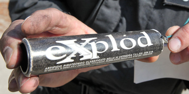 Zwei Hände, die einen schwarzen Böller mit dem weißen Schriftzug "Explod" halten.