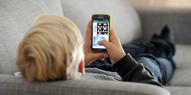 Ein Kind liegt auf dem Sofa und tippt auf seinem Smartphone