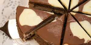 Aus einer Schokoladentorte mit weißen Flecken wird ein Stück mit einem Tortenheber herausgezogen