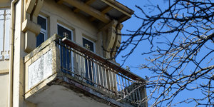 Ein Balkon an dem der Putz bröckelt und sich Moos angesetzt hat.