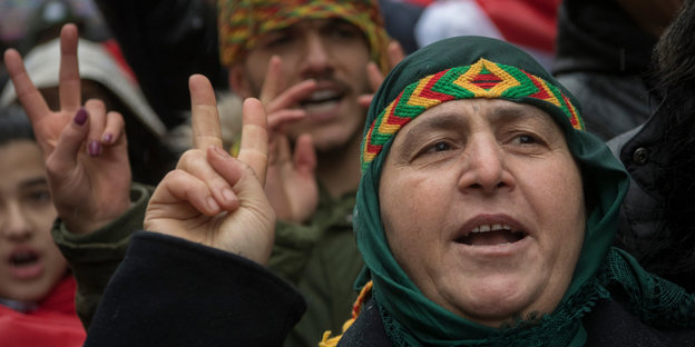 Eine Frau, die ein buntes Stirnband trägt, zeigt das Victory-Zeichen